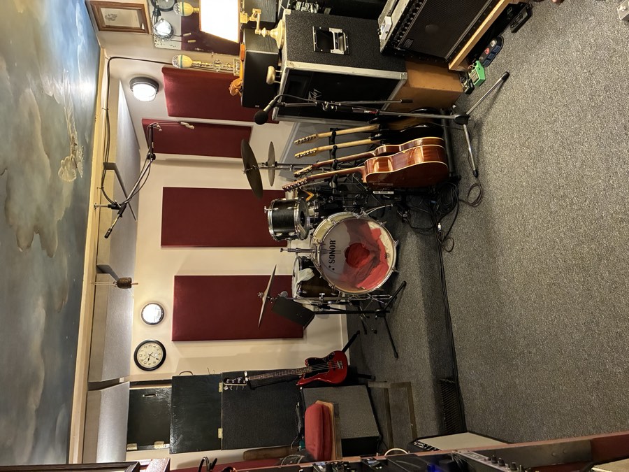 Wide view of the main tracking room with a drum kit, guitars and amps, red acoustic panels and a painted cloud ceiling