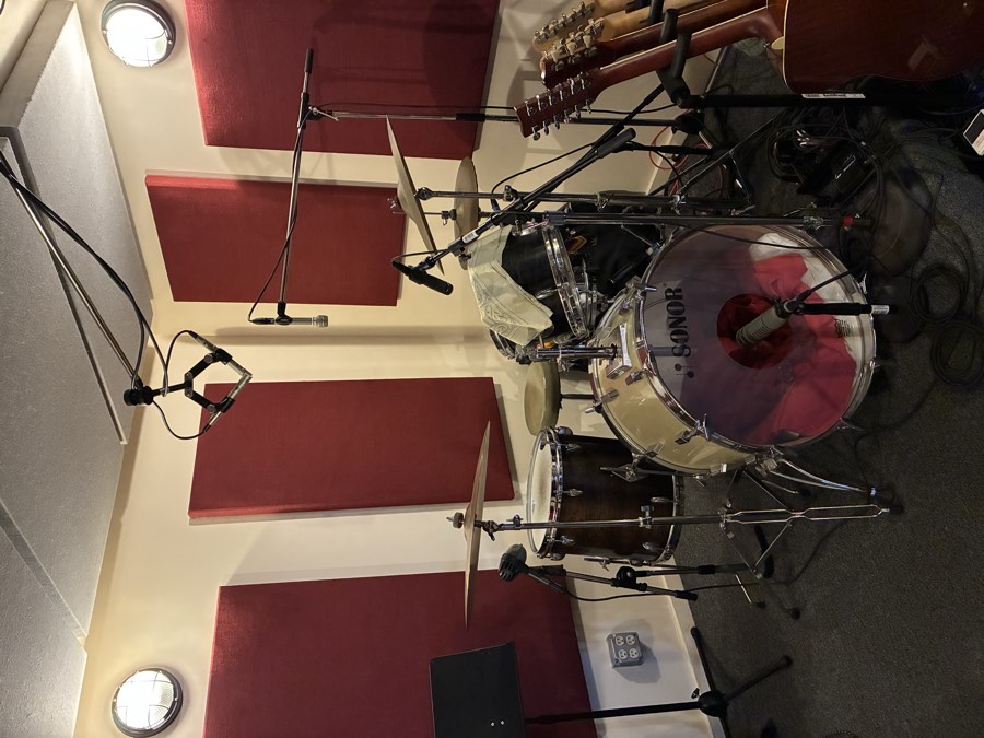 Drum kit with overhead and room microphones in a tracking room lined with red acoustic panels