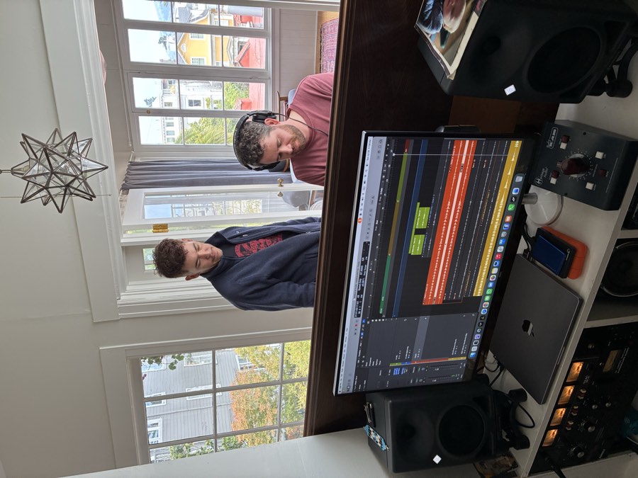 Mixing desk at Milky Mountain Studio with a computer monitor showing a DAW session, studio monitors, and sunlit windows overlooking neighboring rooftops